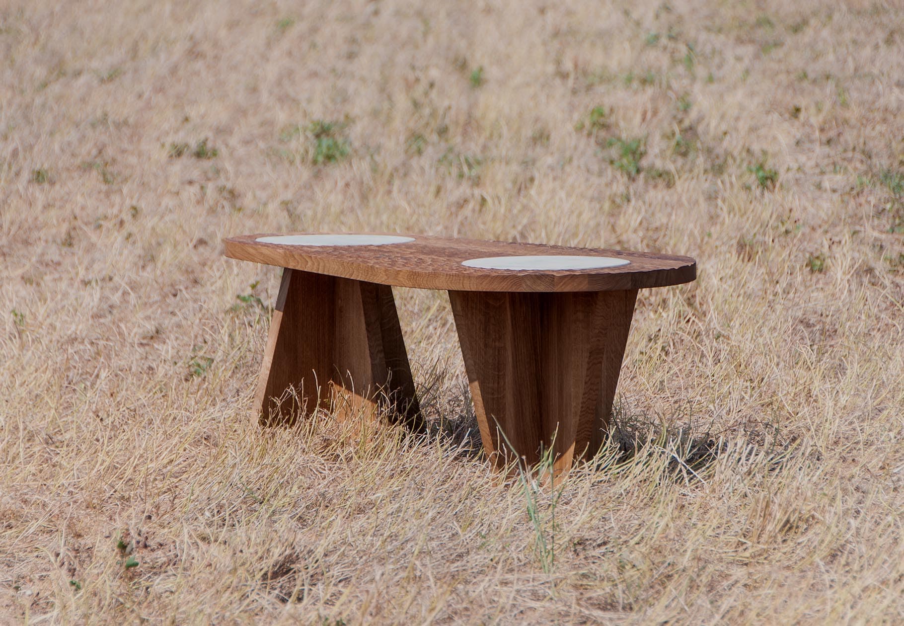 Table basse en chêne brut massif design Plié Architectes. Vue complète montrant le plateau sculpté et les pieds cruciformes robustes.