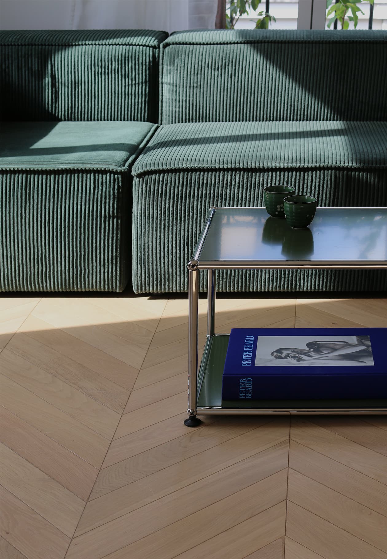 Parquet en chêne en pointe de Hongrie de l’appartement Martinique à Paris, baigné par un rayon de soleil, avec table et canapé design.