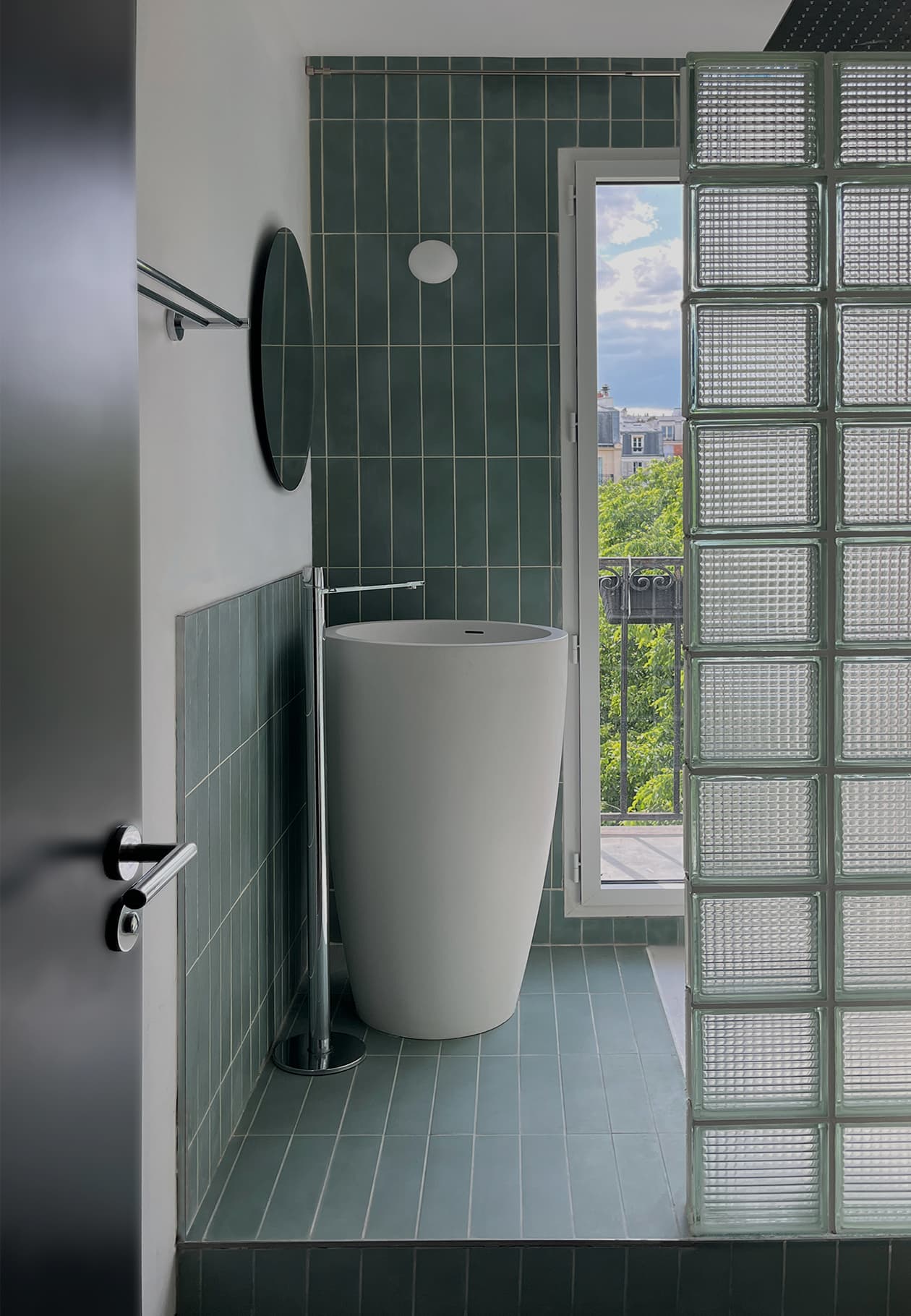 Salle de bain de l’appartement Martinique : cloison de douche en pavé de verre, vasque monolithique et jeux de lumière sur les matériaux.