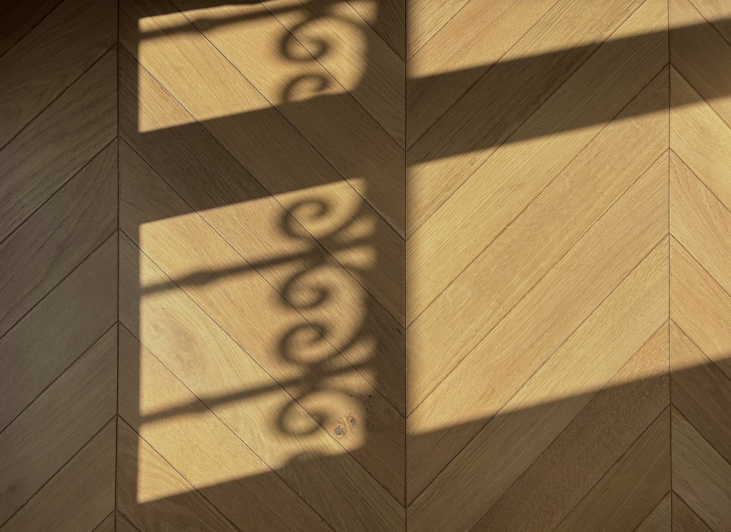 Jeux d’ombre des ferronneries des garde-corps sur le parquet en pointe de Hongrie de l’appartement Martinique à Paris.